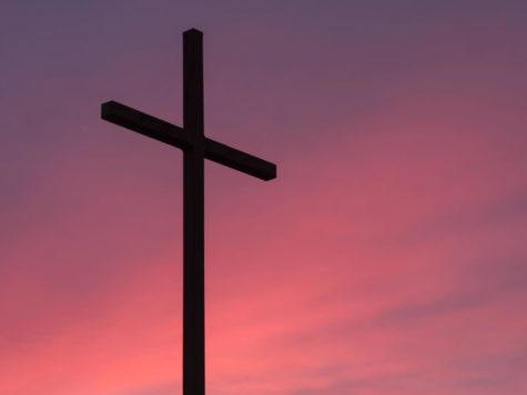 Silhouette of a cross with a pink and purple sunset background