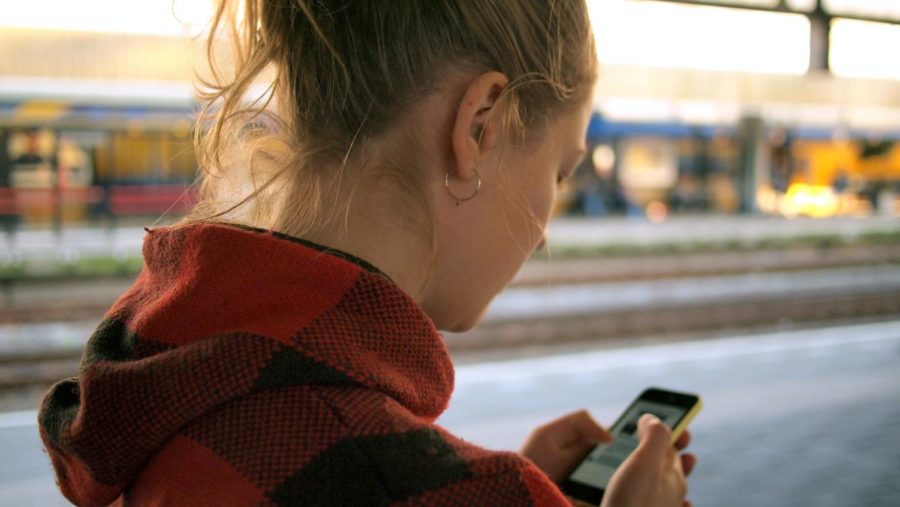 A teen using her phone in front of a blurred outdoor background