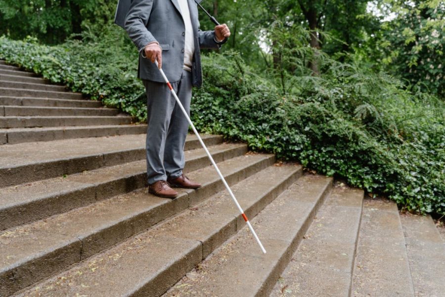 Man in suit is walking down stairs outdoors with a white cane