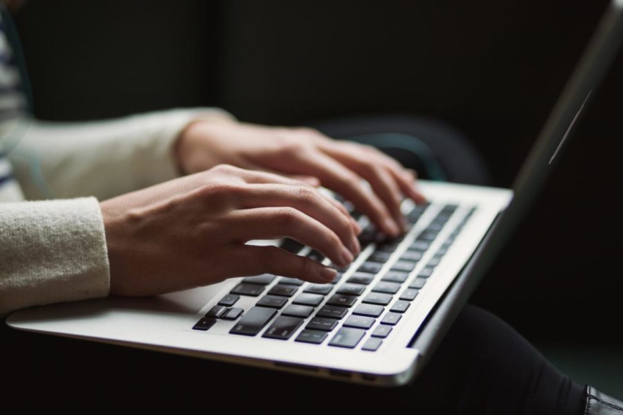 A shot of a laptop with a persons hands typing on the keyboard.