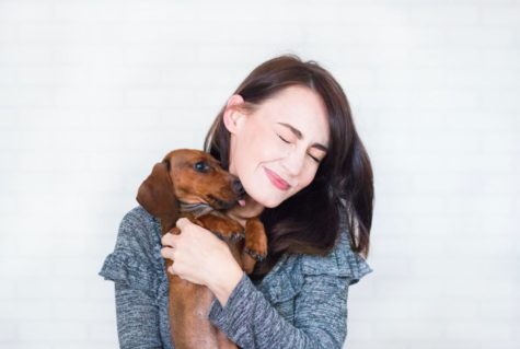 A woman holding a dog against her and hugging it.